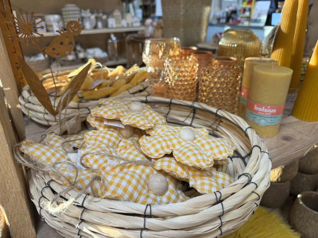 Gelb-weiß-karierte Blumenanhänger und gelbe Kerzen von Bolsius in der Landfuxx Dekoabteilung.